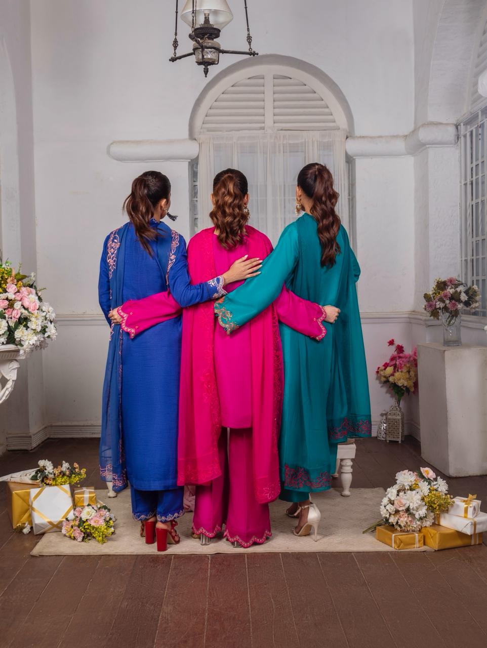 Three women in colorful traditional outfits standing together in a decorated room.